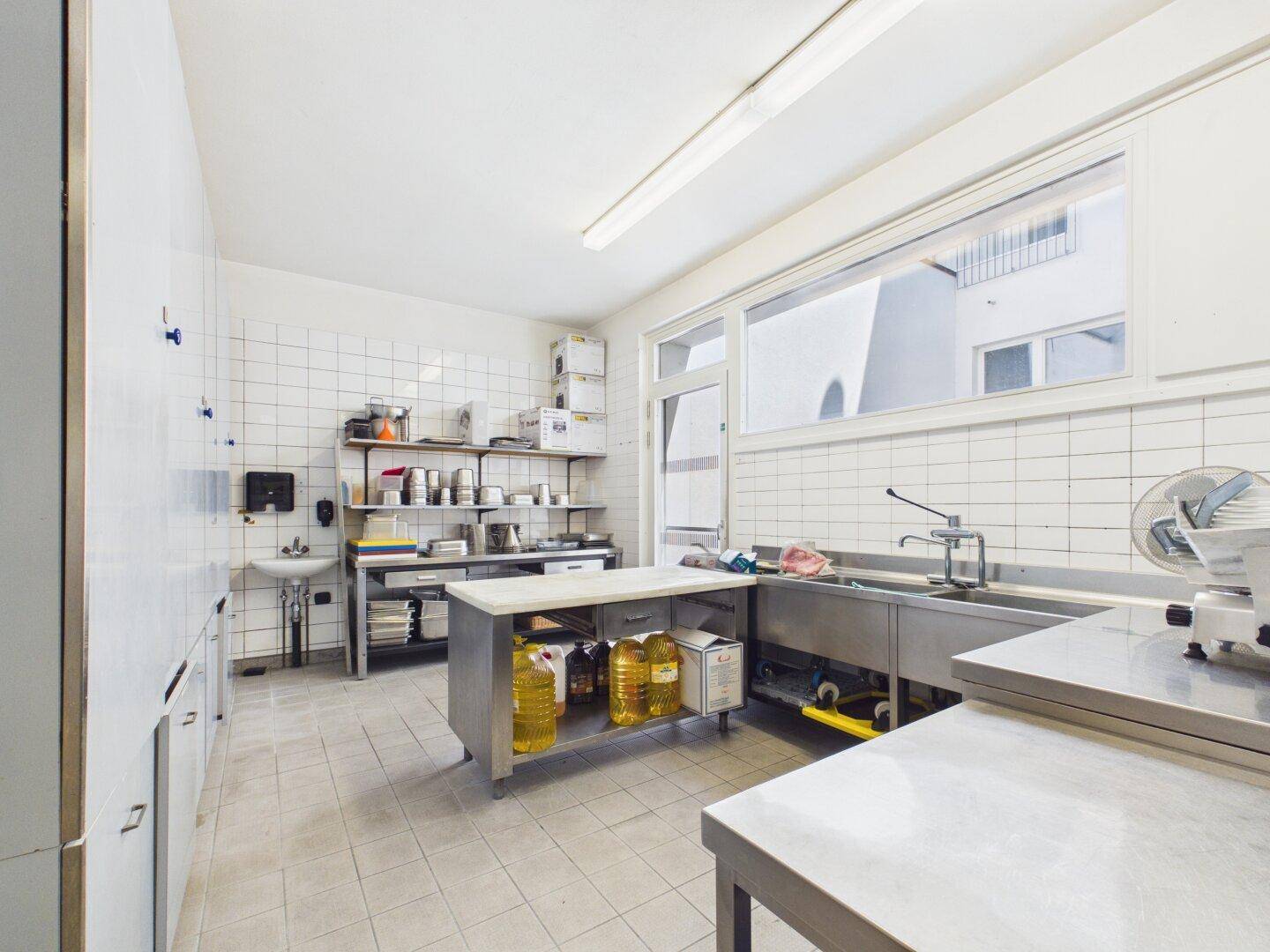 Helle Großküche mit Fenster, Edelstahlspüle und Arbeitsflächen, bereit für den professionellen Einsatz.