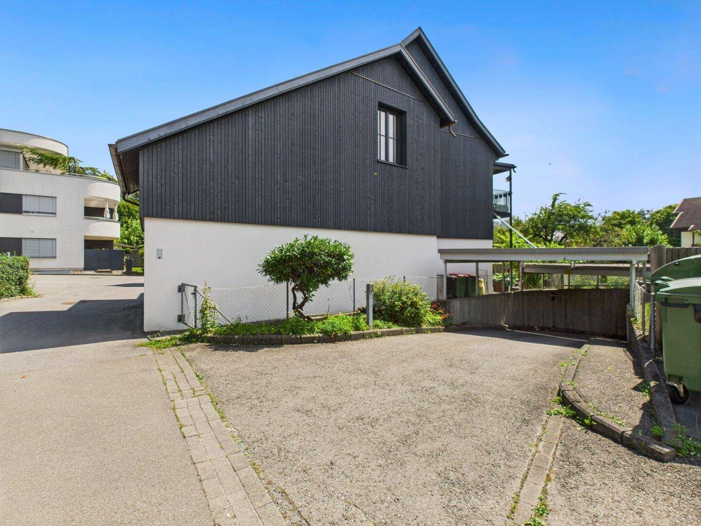 Seitenansicht eines modernen Gebäudes mit dunkler Holzfassade und Parkplatz.