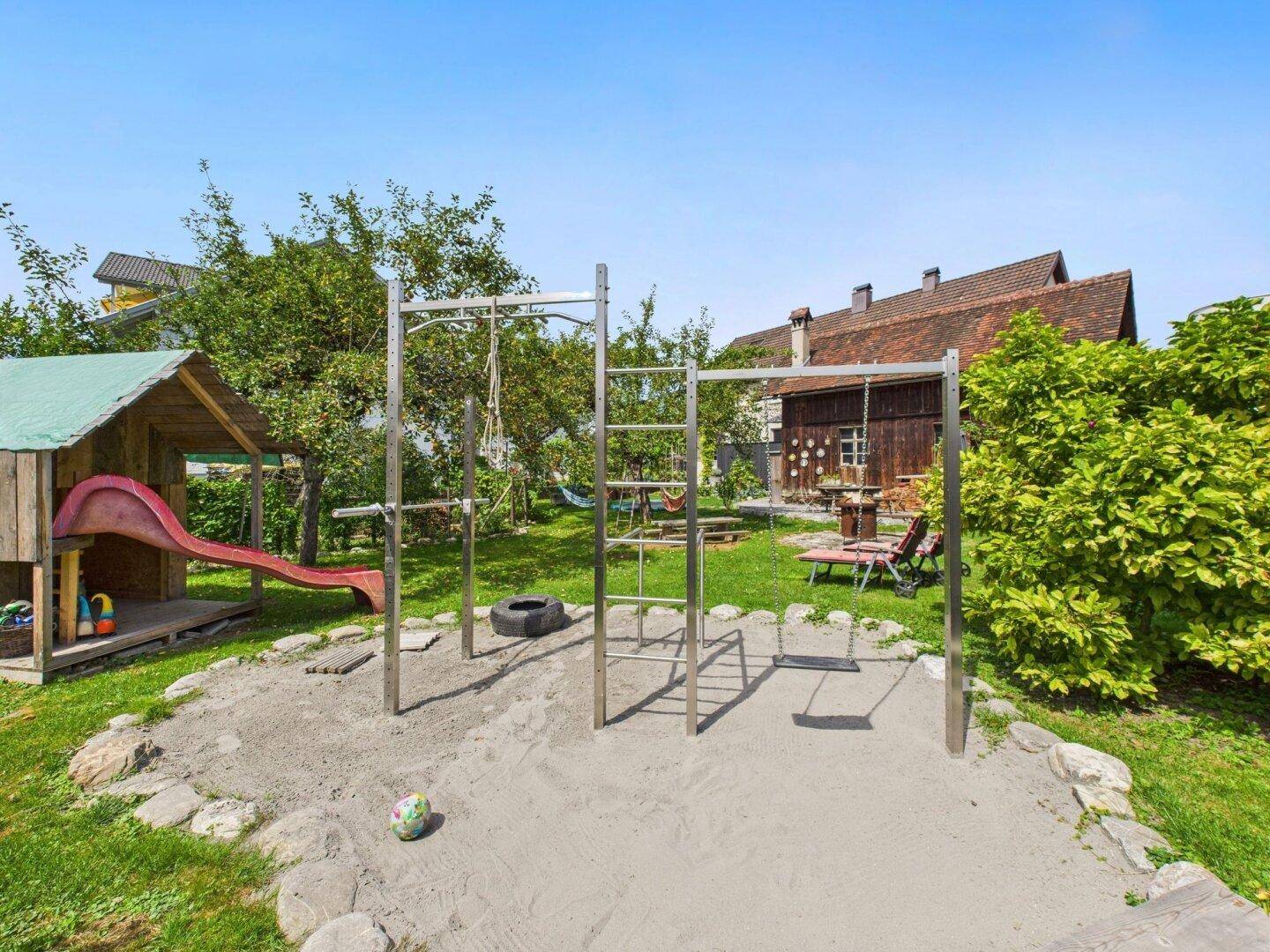Sandkastenbereich im Garten mit Klettergerüst, Rutsche und Spielhaus für Kinder.