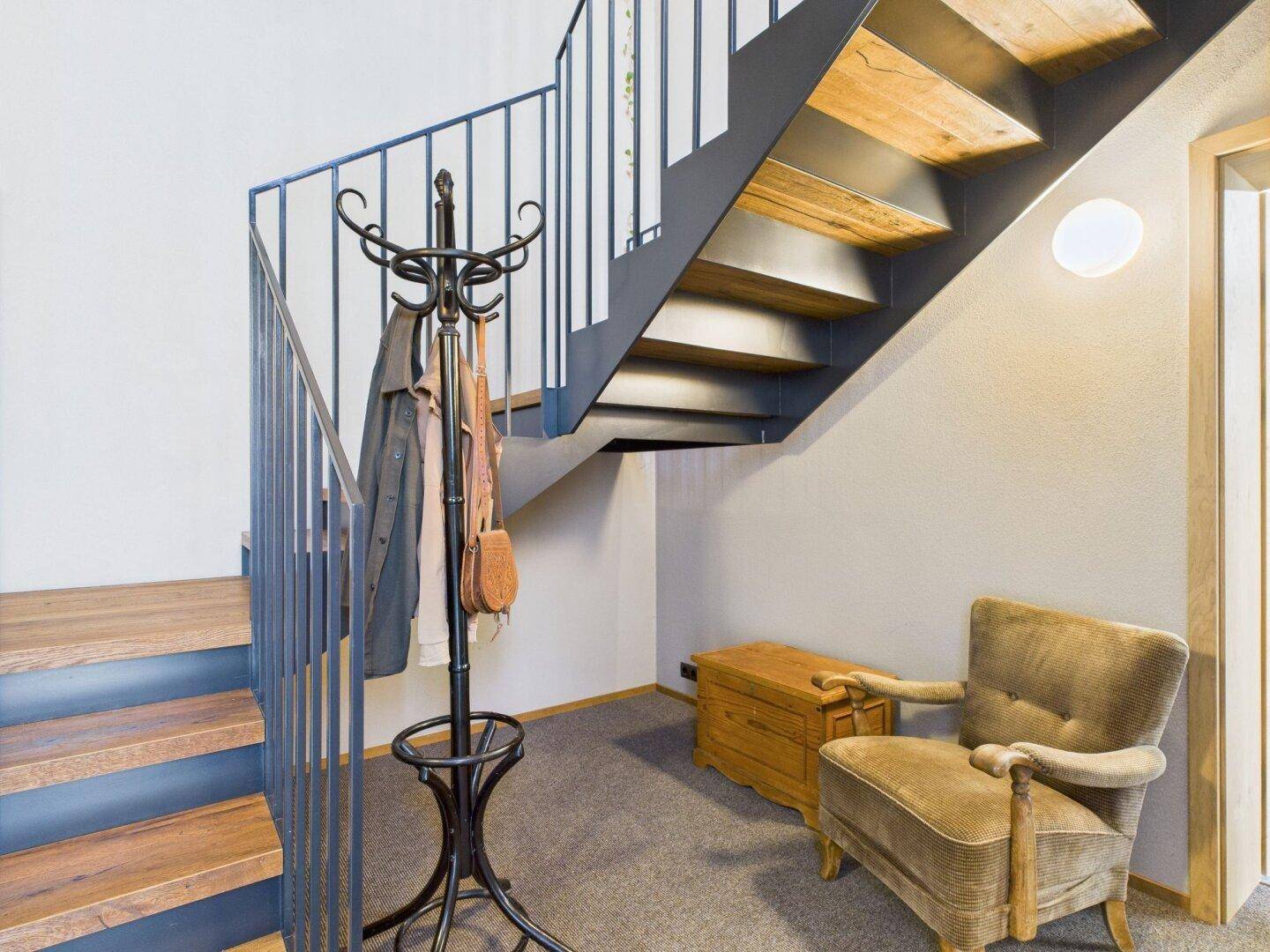 Heller Flur mit moderner Holztreppe, Metallgeländer und Garderobenständer.