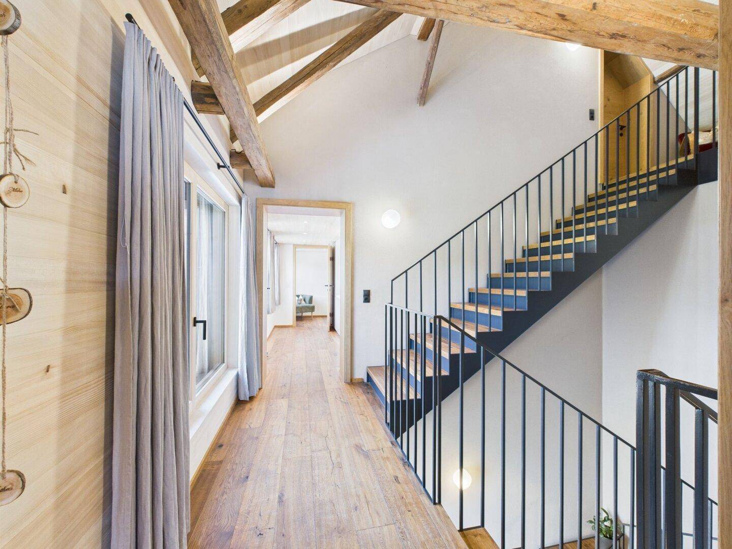 Heller Flur mit Holzfußboden, Holzbalkendecke und einer modernen Treppe.