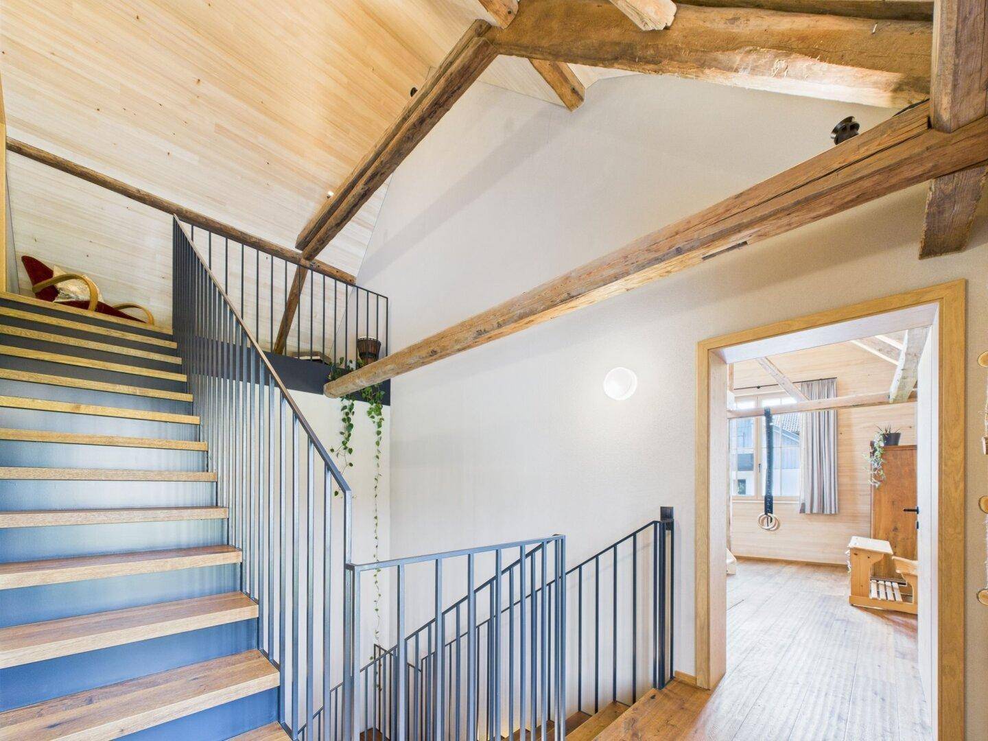 Moderne Treppe mit Holzstufen und Metallgeländer, die zu einem offenen Bereich führt.