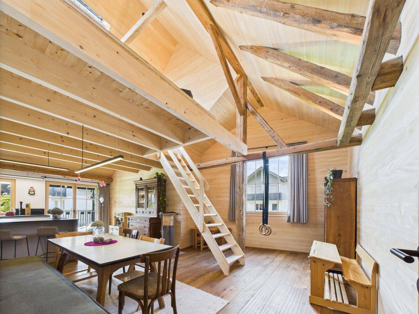 Geräumiger Wohnbereich mit hoher Holzbalkendecke, Esstisch und einer Leiter zum Dachboden.