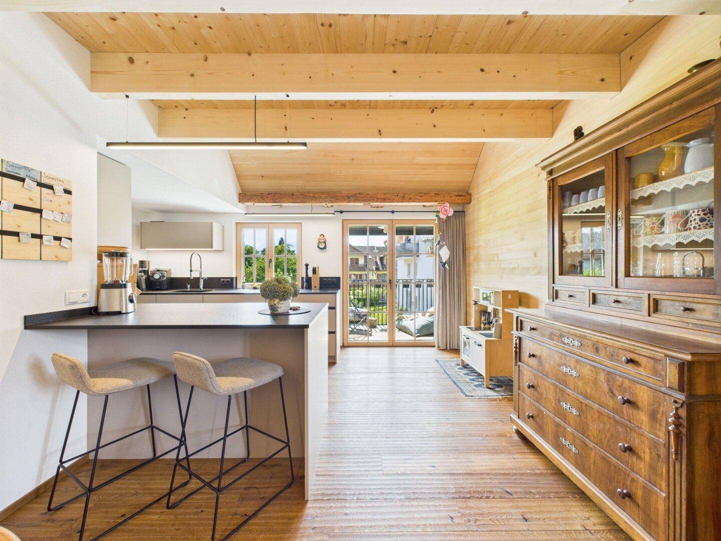 Moderne Küche mit Holzbalkendecke, Kücheninsel und Zugang zu einem sonnigen Balkon.