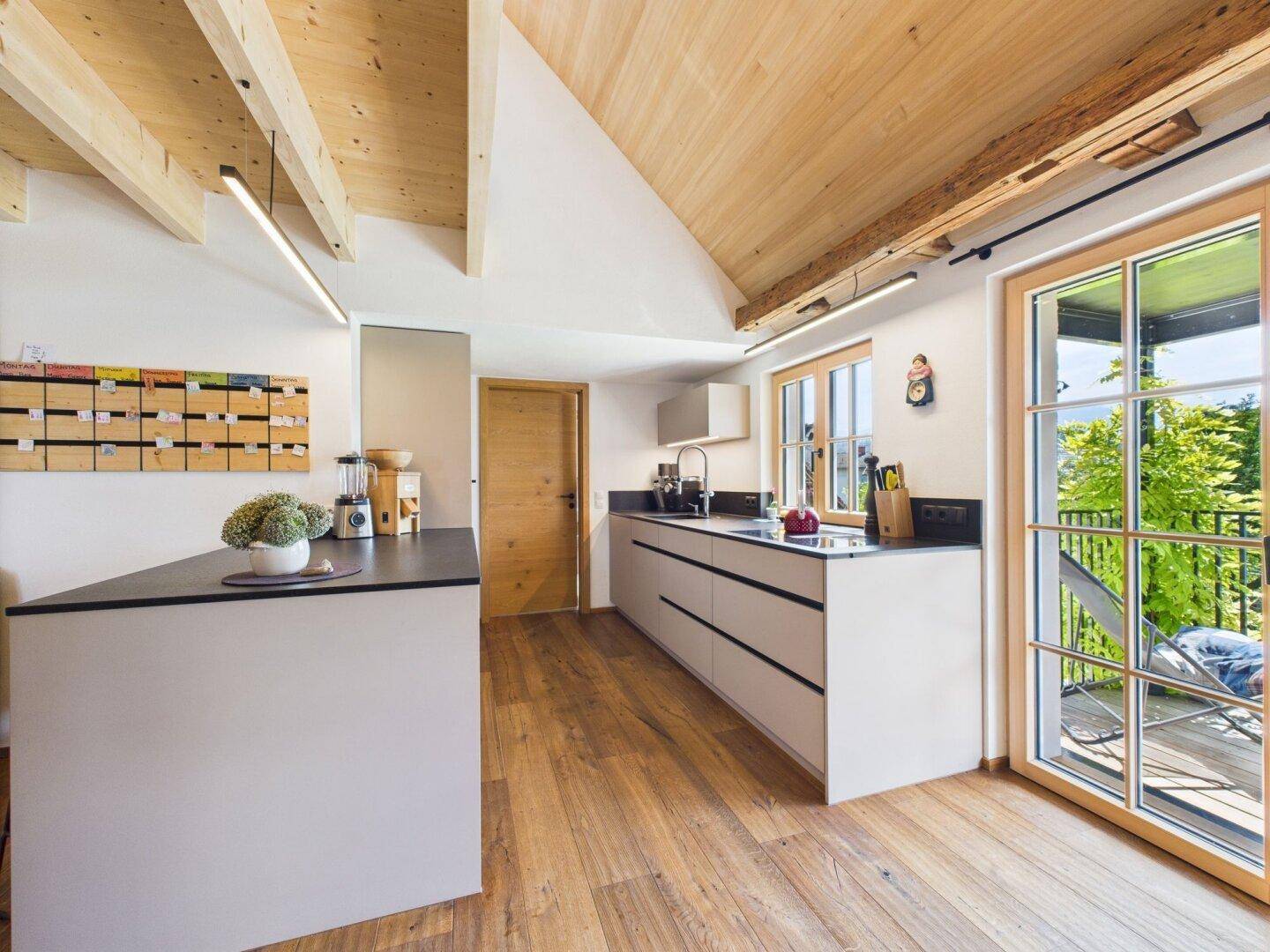 Helle Küche mit modernen Schränken, Holzbalkendecke und Zugang zum Balkon.