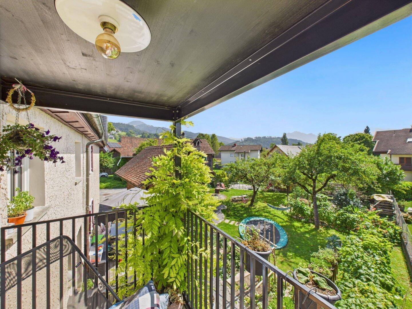 Balkon mit weitem Blick über einen grünen Garten und die umliegende Berglandschaft.