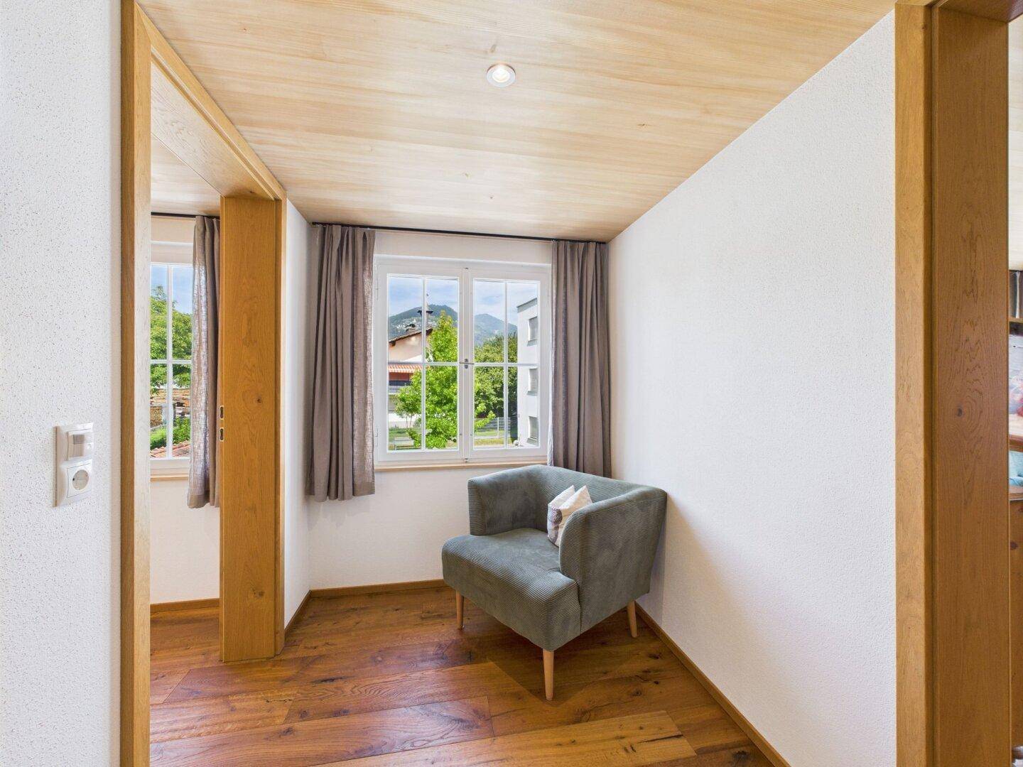 Kleiner Raum mit Sessel, Holzboden und einem Fenster mit Bergblick.