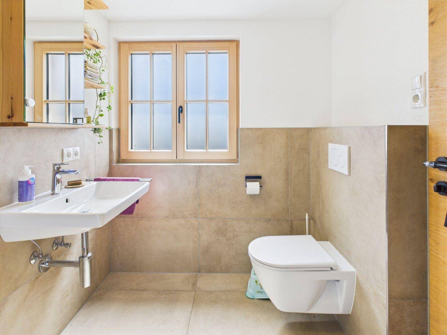 Modernes Badezimmer mit Waschbecken, wandhängendem WC und einem Fenster für Tageslicht.