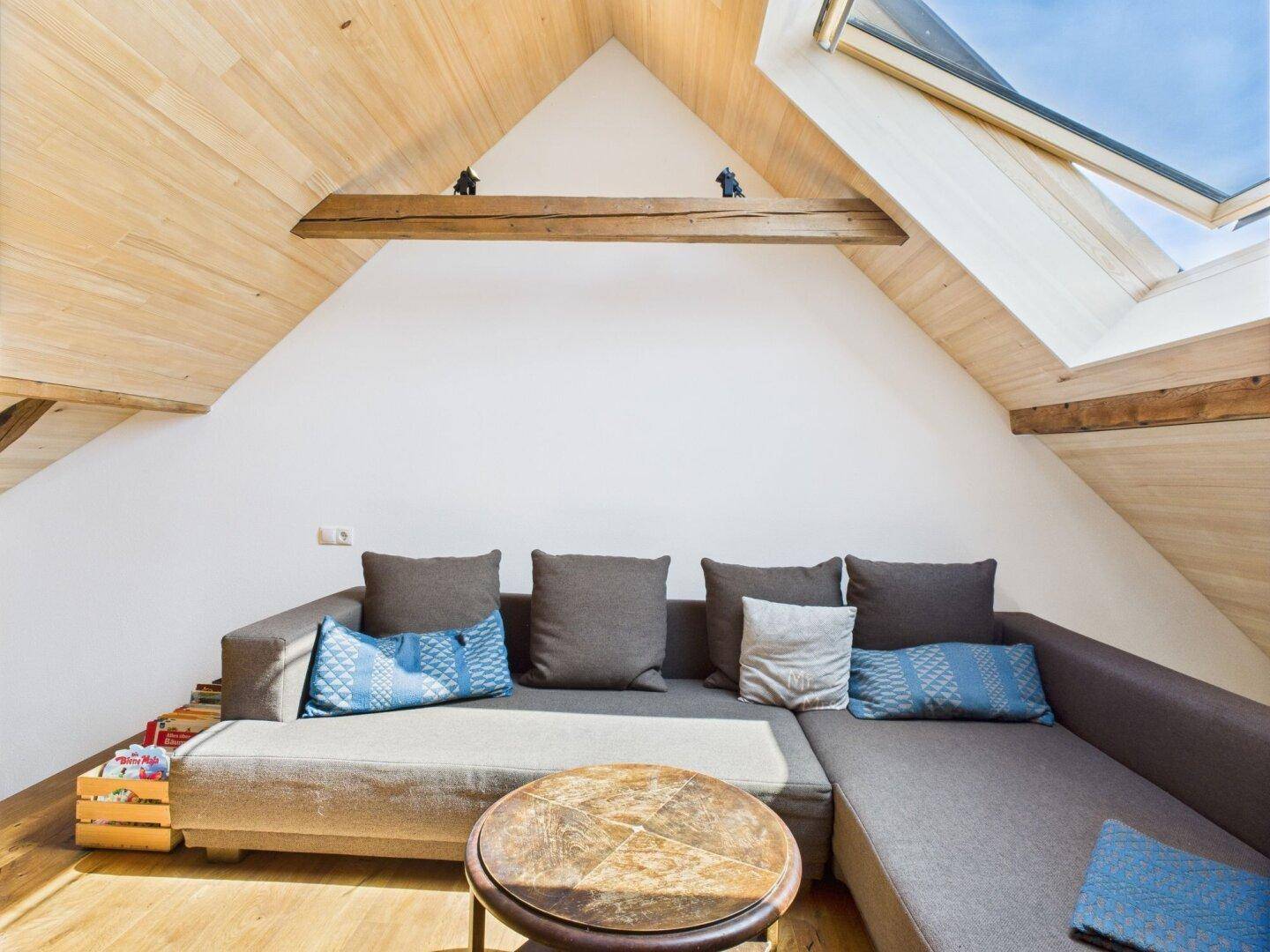 Gemütlicher Wohnbereich unter dem Dach mit Dachfenster, großem Sofa und Holzboden.