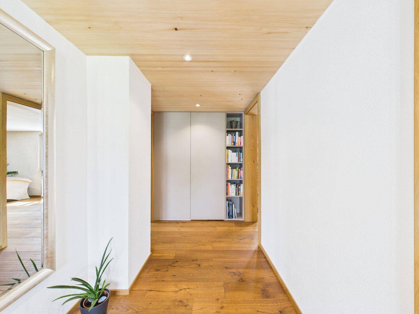 Geräumiger Flur mit Holzboden, Holzbalkendecke und integrierten Bücherregalen.