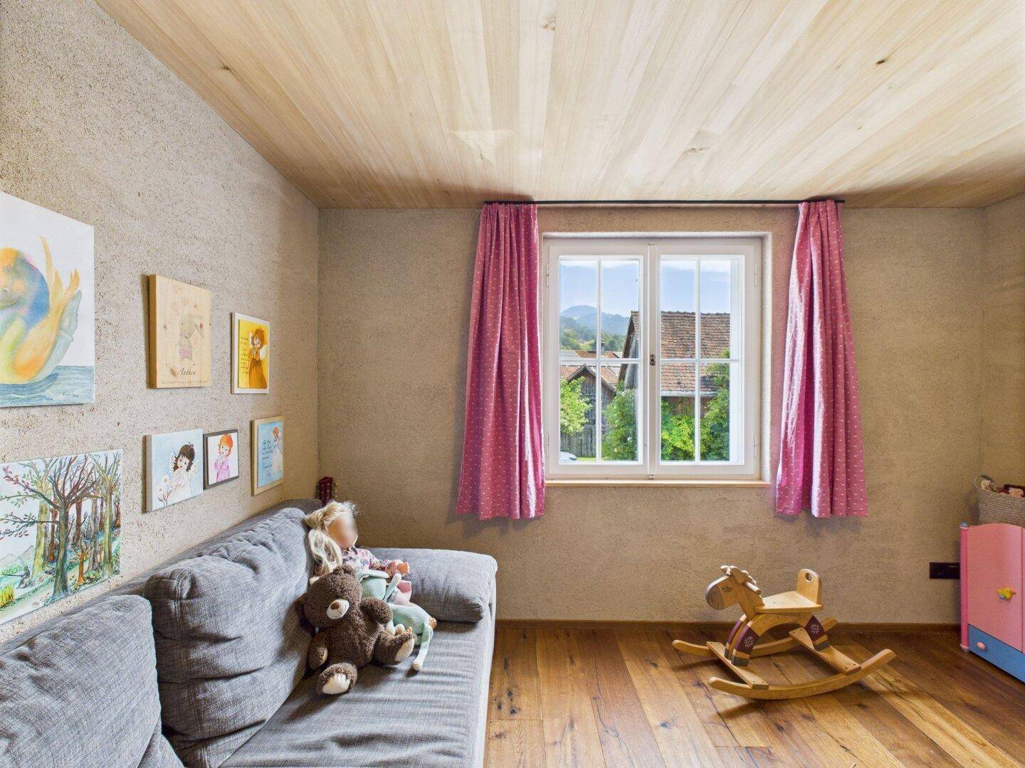 Kinderzimmer mit Sofa, Schaukelpferd und einem Fenster mit Blick ins Grüne.