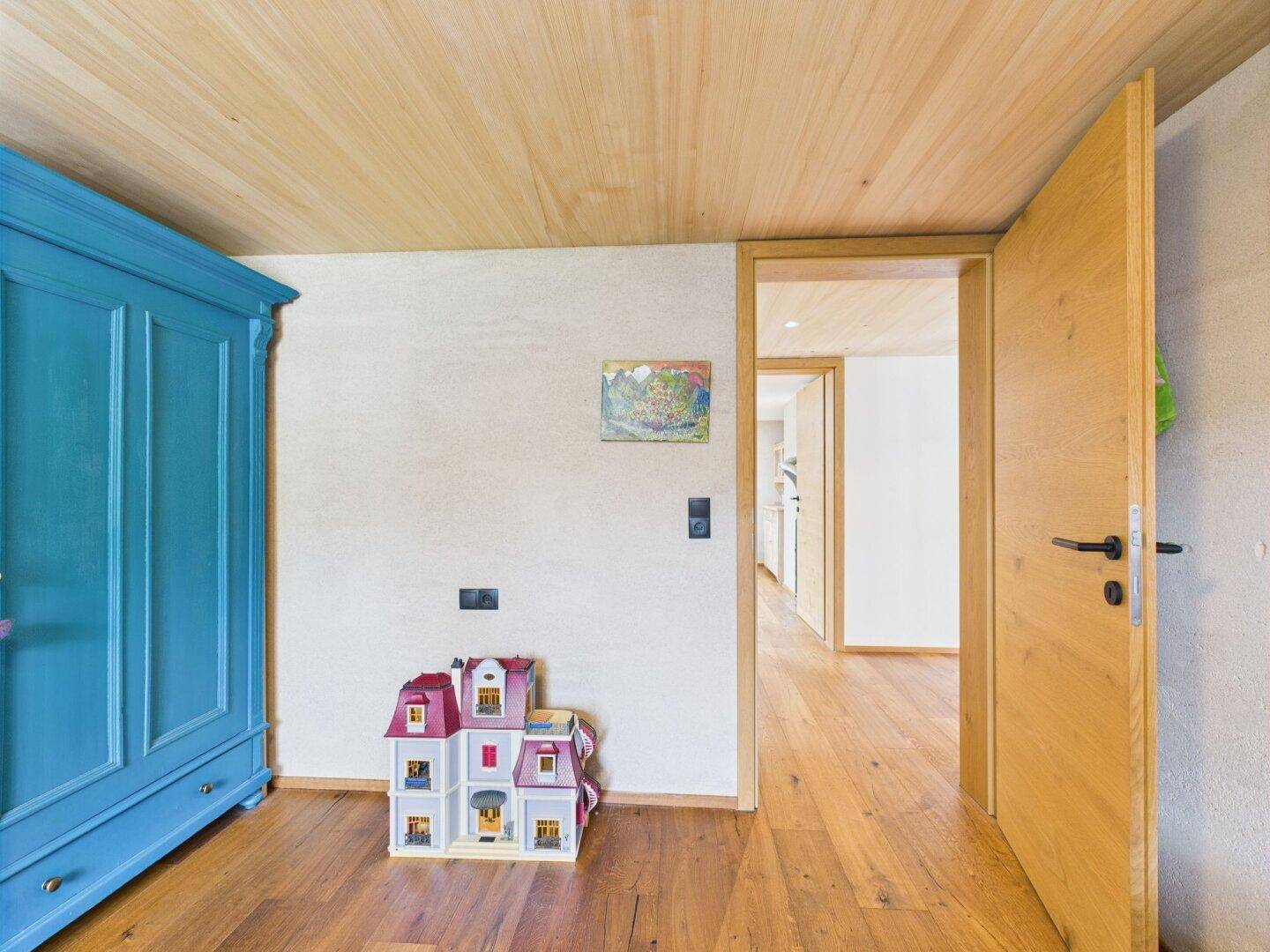 Kinderzimmer mit blauem Kleiderschrank, Puppenhaus und Holzboden.