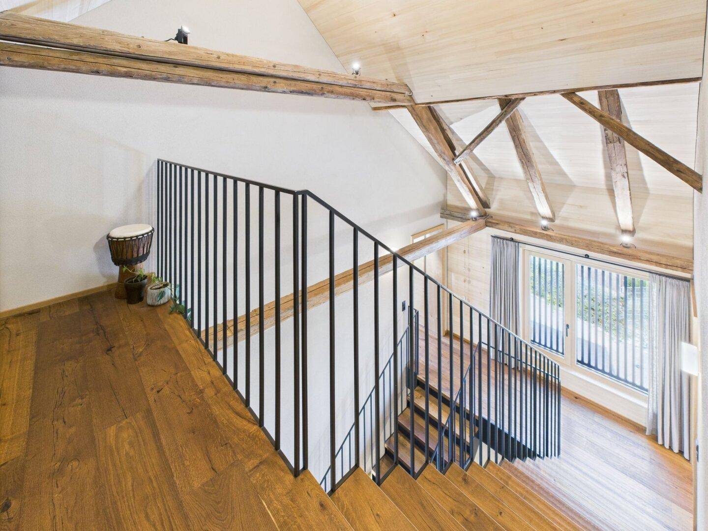 Moderne Holztreppe mit schwarzem Metallgeländer und Blick auf ein Fenster.