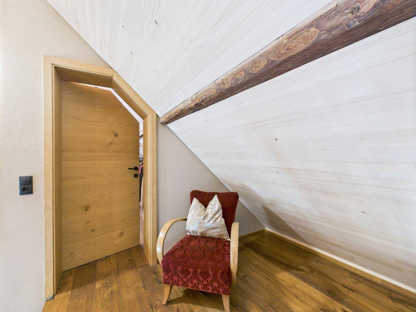 Gemütlicher Bereich unter dem Dach mit Sessel und Holztür.