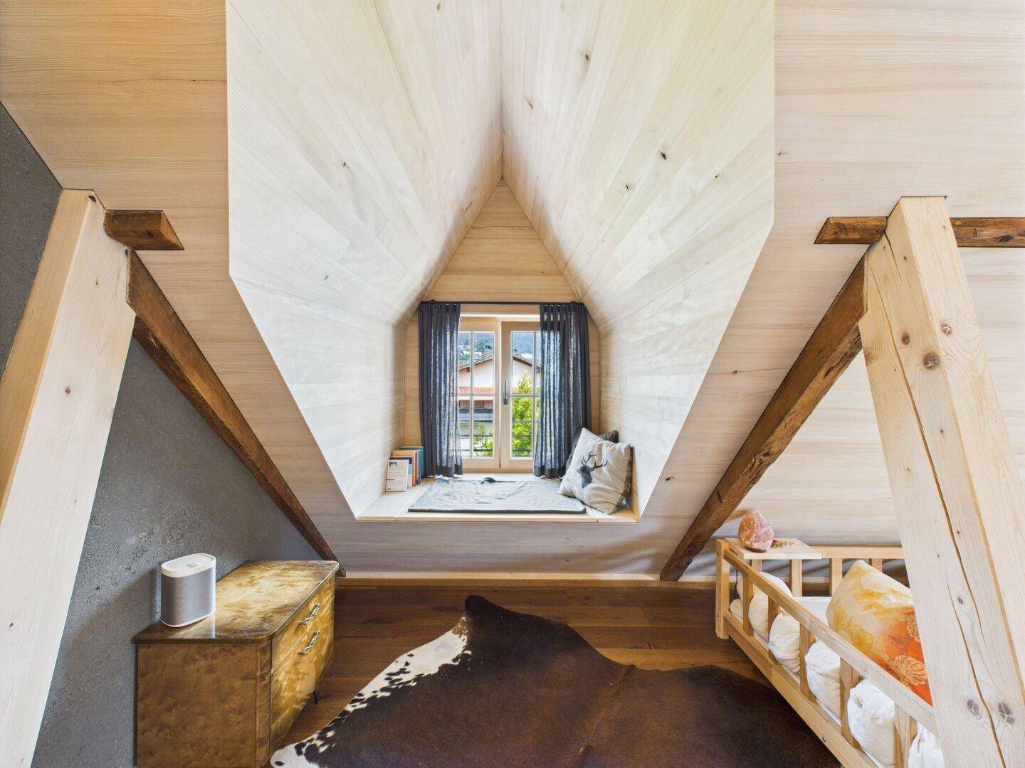 Gemütliches Schlafzimmer im Dachgeschoss mit Holztäfelung, Dachschräge und einem Fenster mit Ausblick.