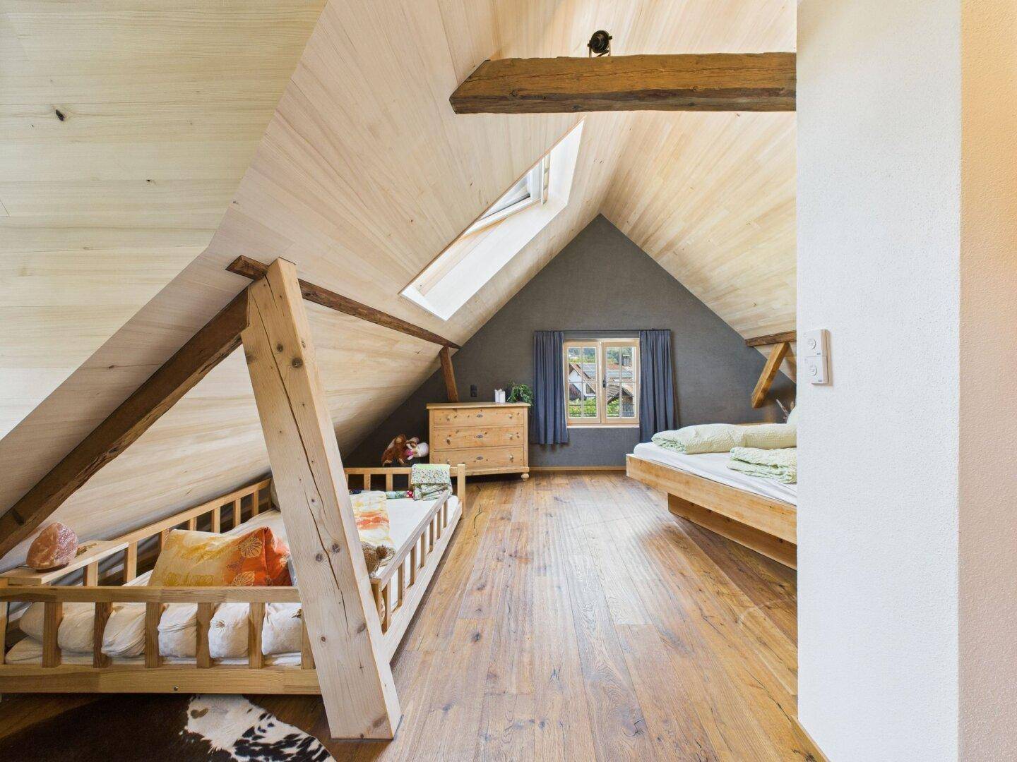Helles Schlafzimmer im Dachgeschoss mit Holzboden, Dachfenster und zwei Betten.