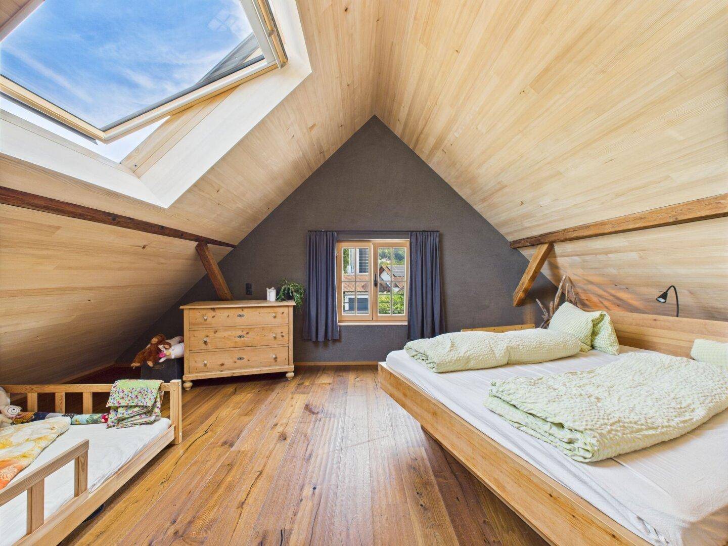Geräumiges Schlafzimmer im Dachgeschoss mit Holzboden, Dachfenster und Blick ins Grüne.