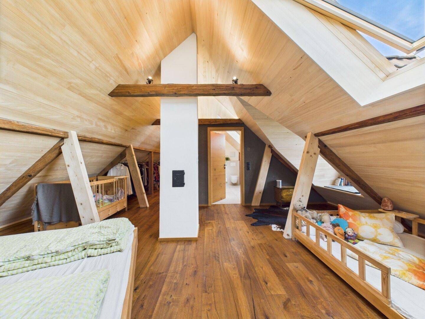 Offener Schlafbereich im Dachgeschoss mit Holzboden, Dachschräge und Zugang zu weiteren Räumen.