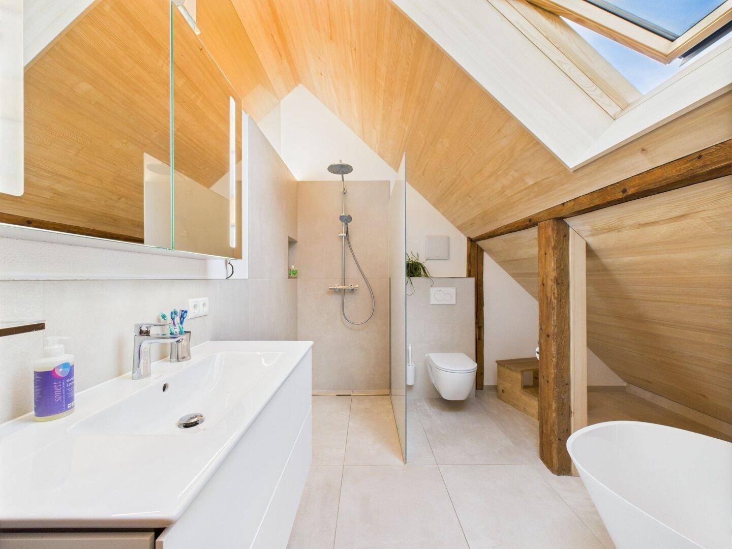 Helles Badezimmer im Dachgeschoss mit Waschtisch, Dusche und Dachfenster für viel Tageslicht.