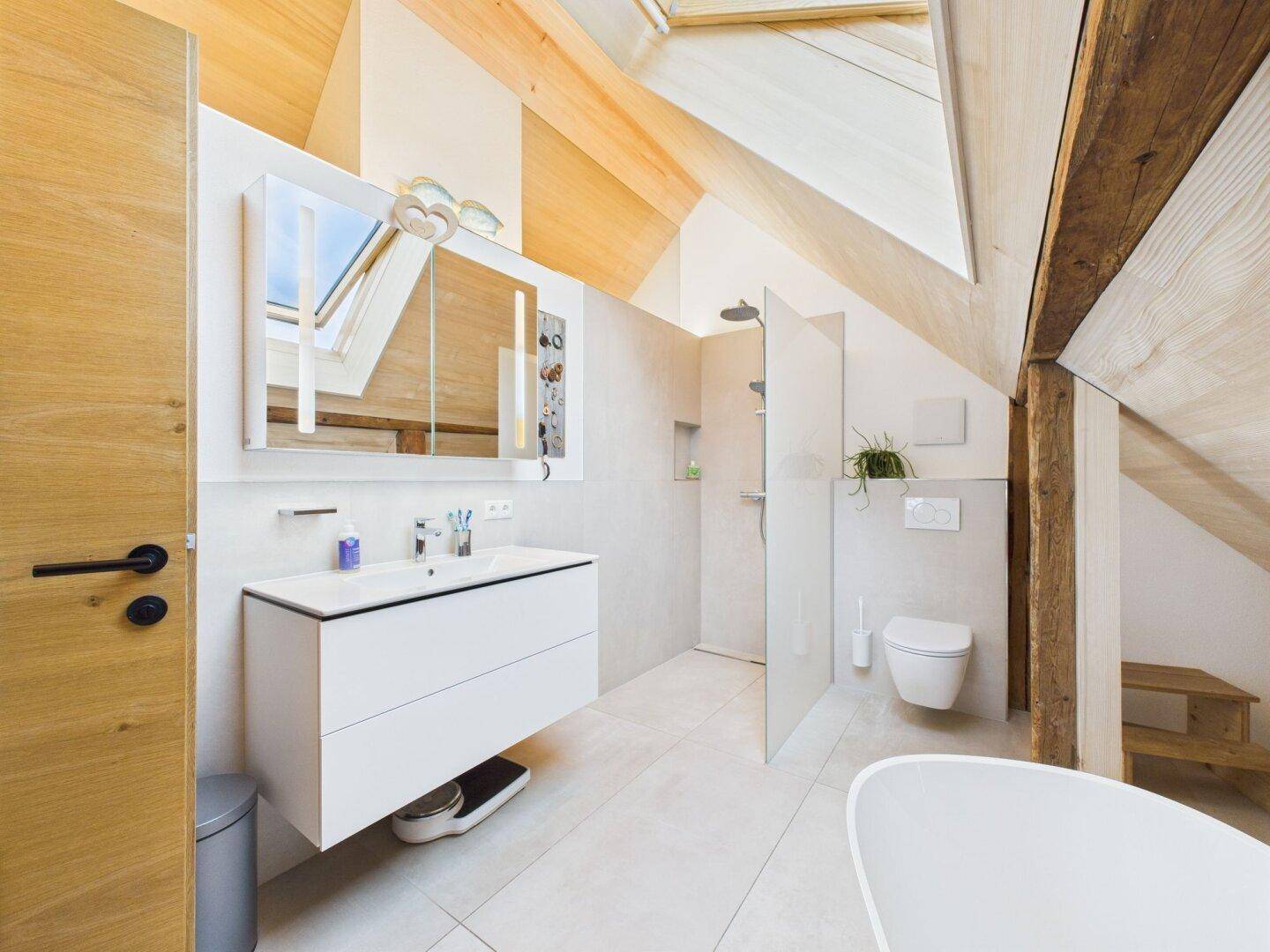 Geräumiges Badezimmer im Dachgeschoss mit modernem Waschtisch, Dusche und freistehender Badewanne.