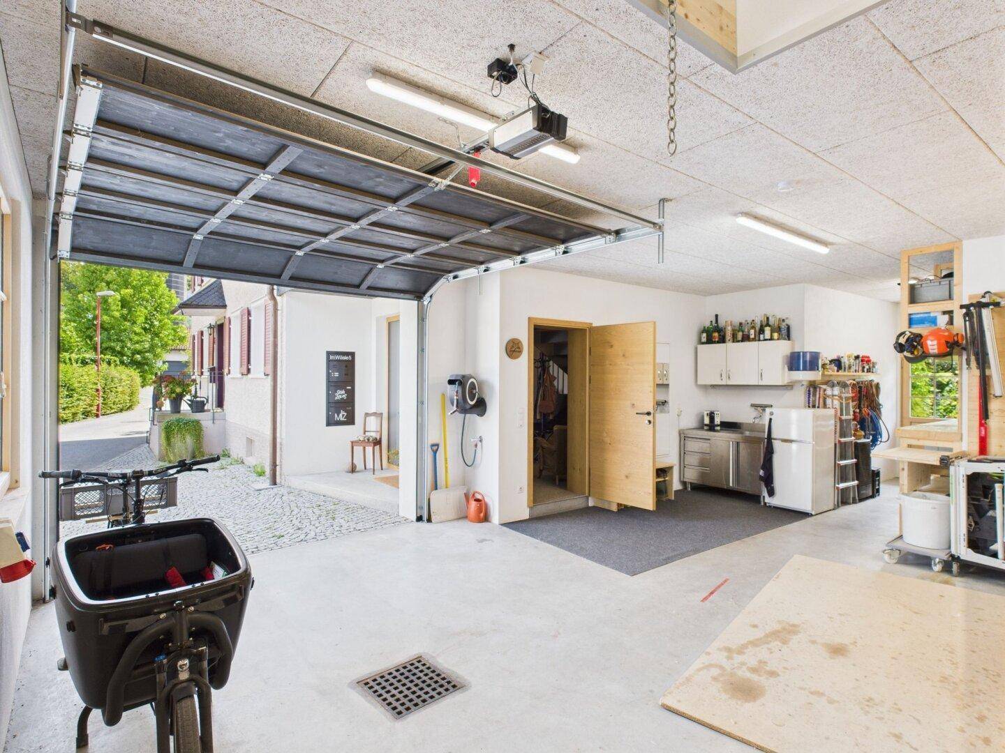 Geräumige Garage mit offenem Tor, Werkstattbereich und direktem Zugang zum Außenbereich.