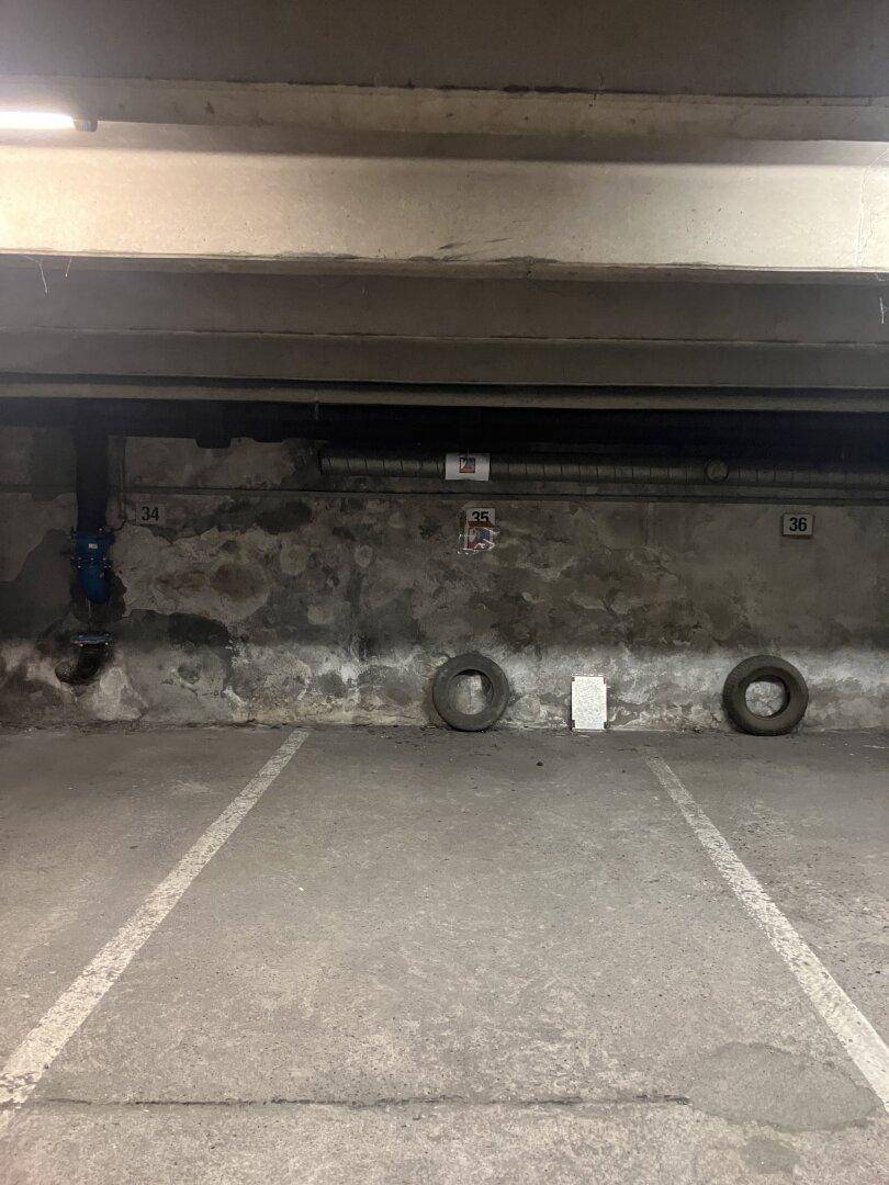Tiefgaragenstellplatz mit Betonboden und sichtbaren Installationen an der Wand.
