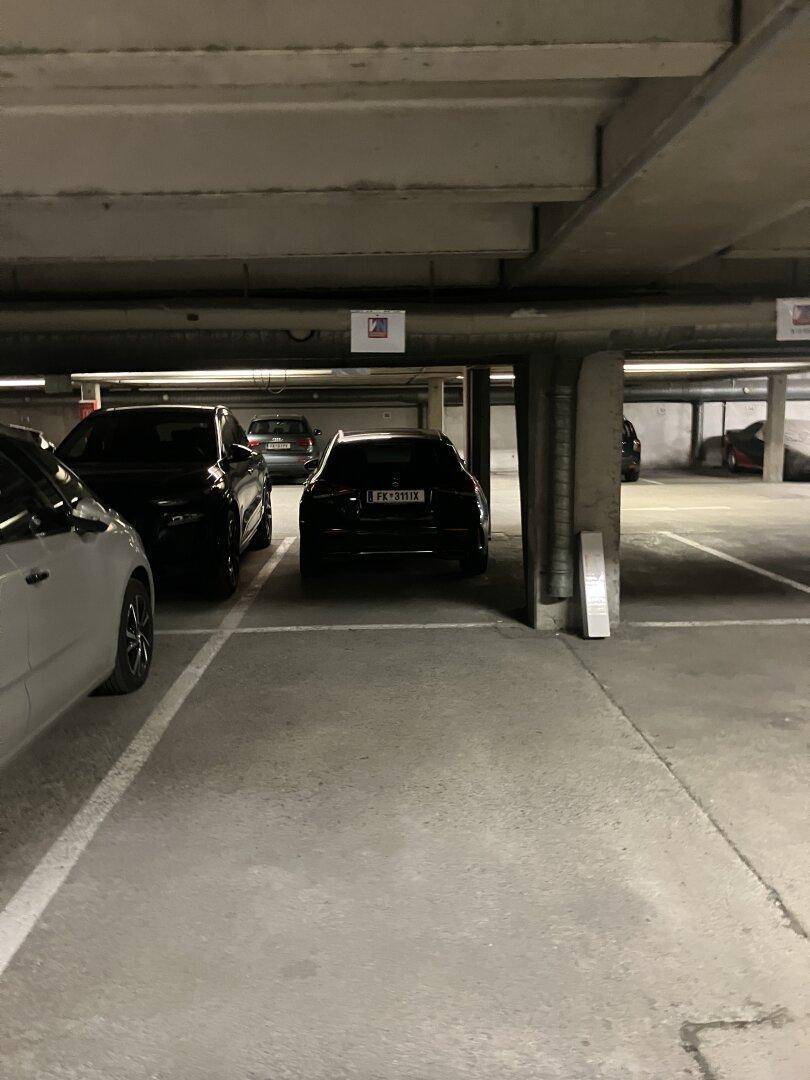 Geräumige Tiefgarage mit mehreren geparkten Fahrzeugen und Betonstützen.