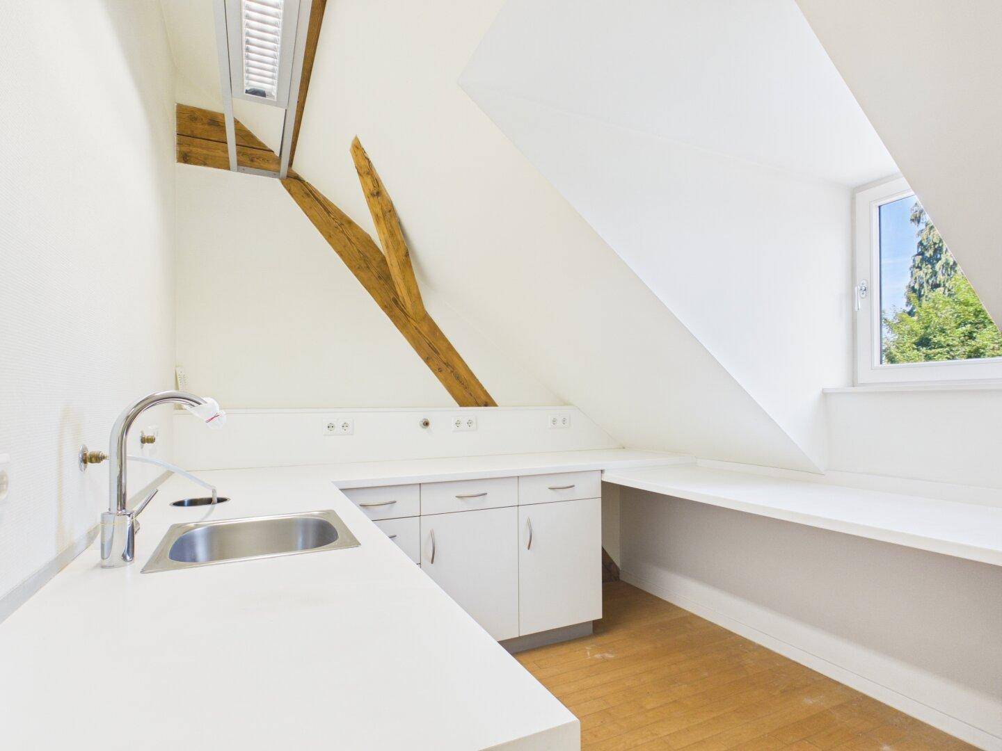 Weißer Büroraum mit Holzbalken, Fenster und integrierter Küchenzeile mit Spüle.