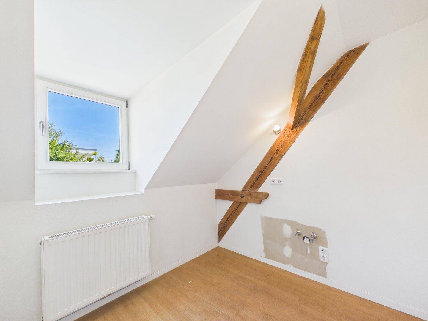 Weißer Büroraum mit Holzbalken, Fenster und Heizkörper.