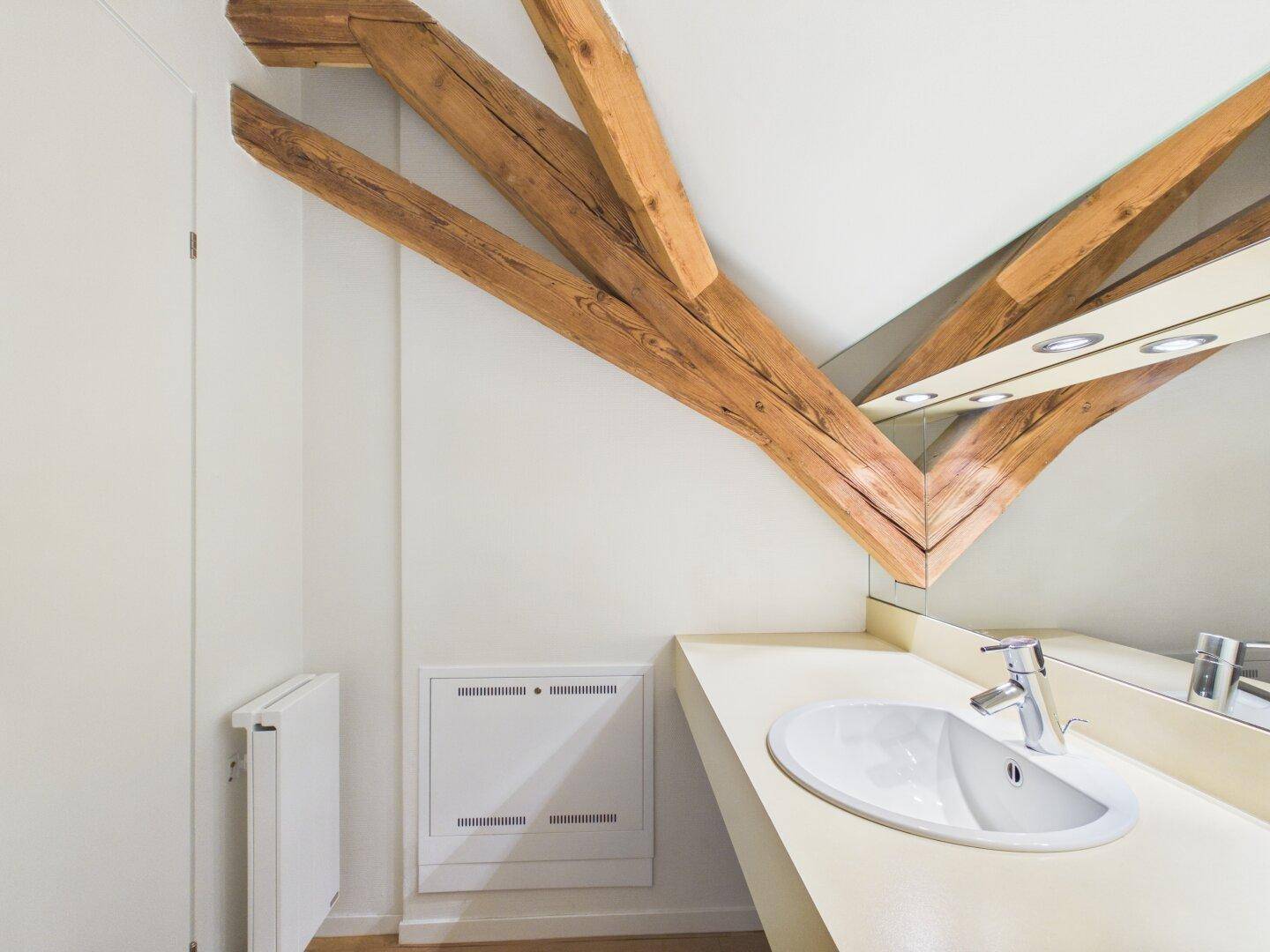 Modernes Badezimmer mit Waschtisch, Spiegel und Holzbalken.