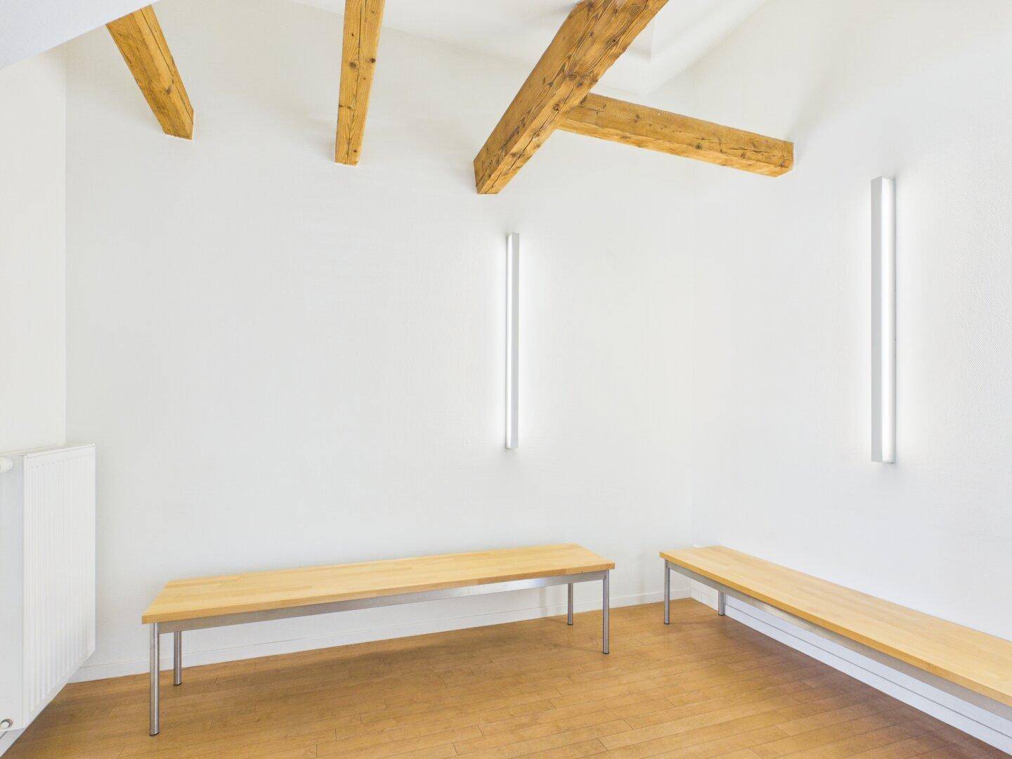 Heller Büroraum mit Holzbalken, weißen Wänden und Holzbänken.