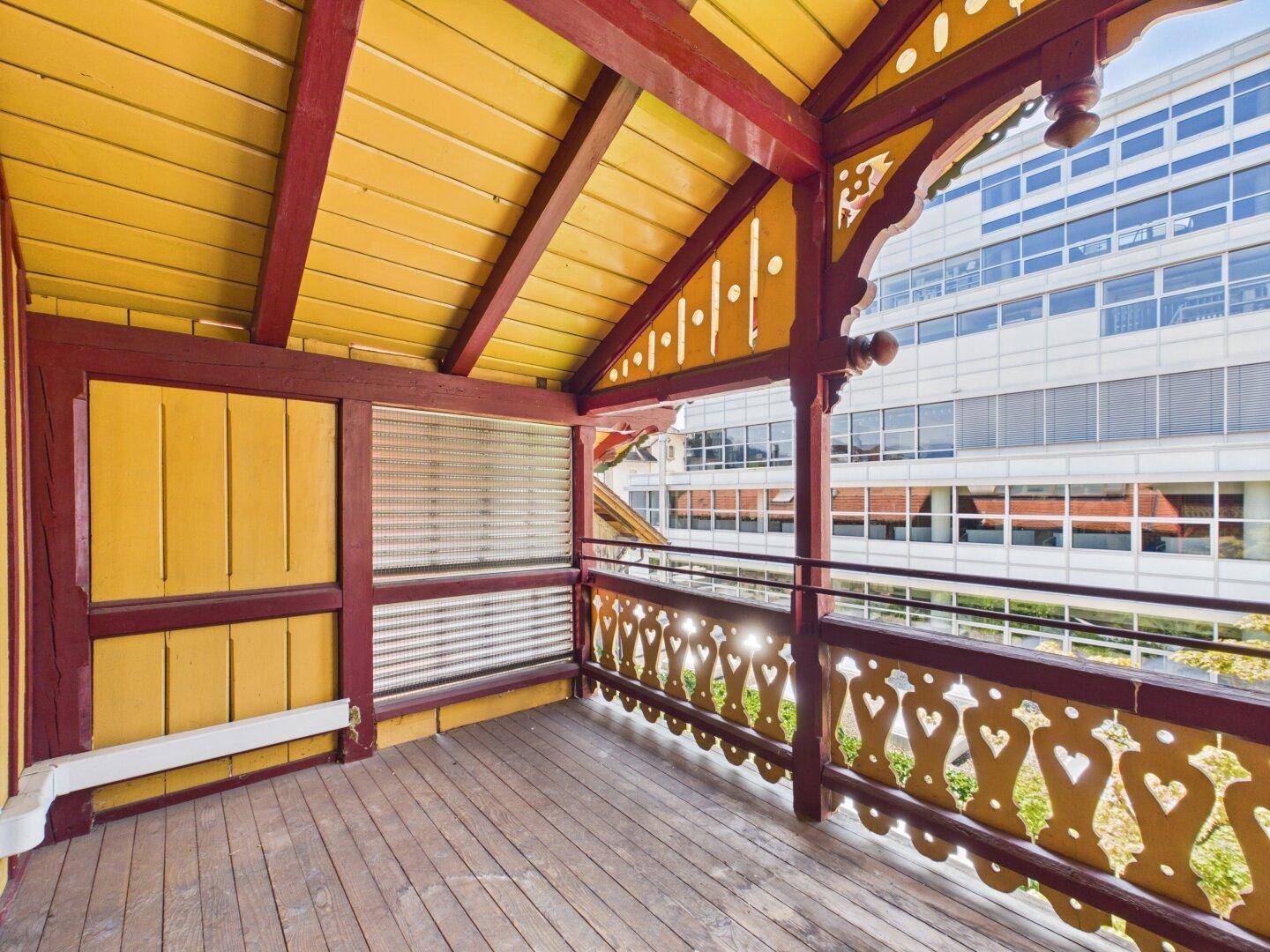 Traditioneller Holzbalkon mit aufwendigen Schnitzereien und Blick auf moderne Gebäude.
