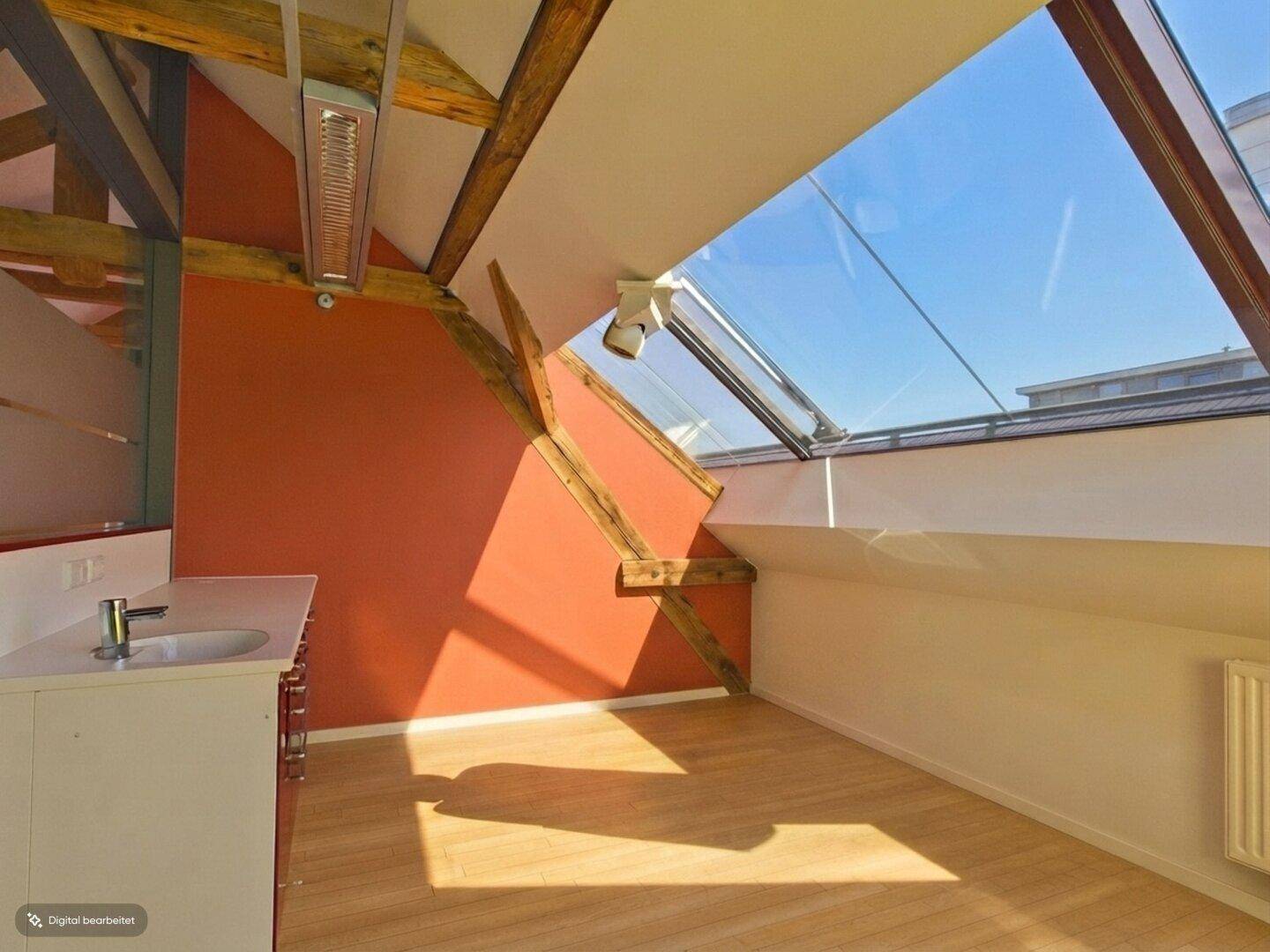Büroraum mit roten Wänden, Holzbalken, großem Dachfenster und integrierter Arbeitsfläche.