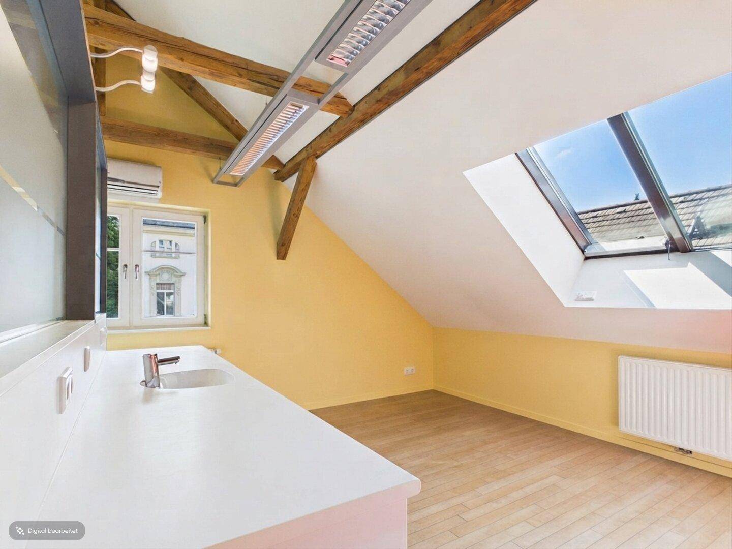 Heller Büroraum mit gelben Wänden, Holzbalken und großem Dachfenster.