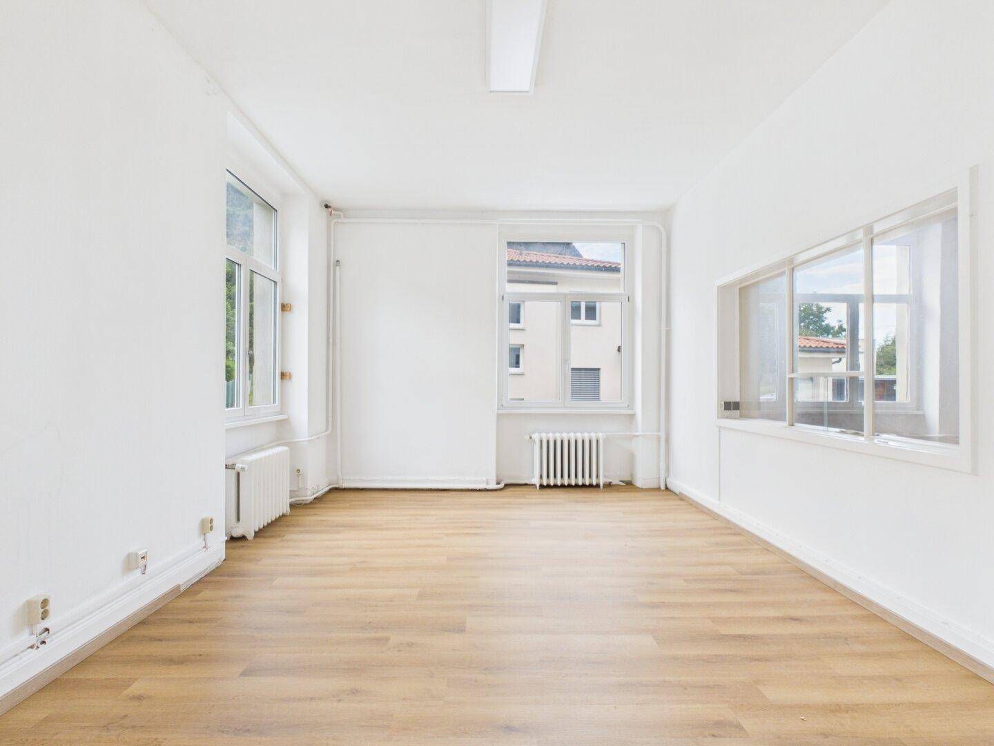 Langer, heller Raum mit mehreren Fenstern und modernem Holzboden, ideal für flexible Nutzung.