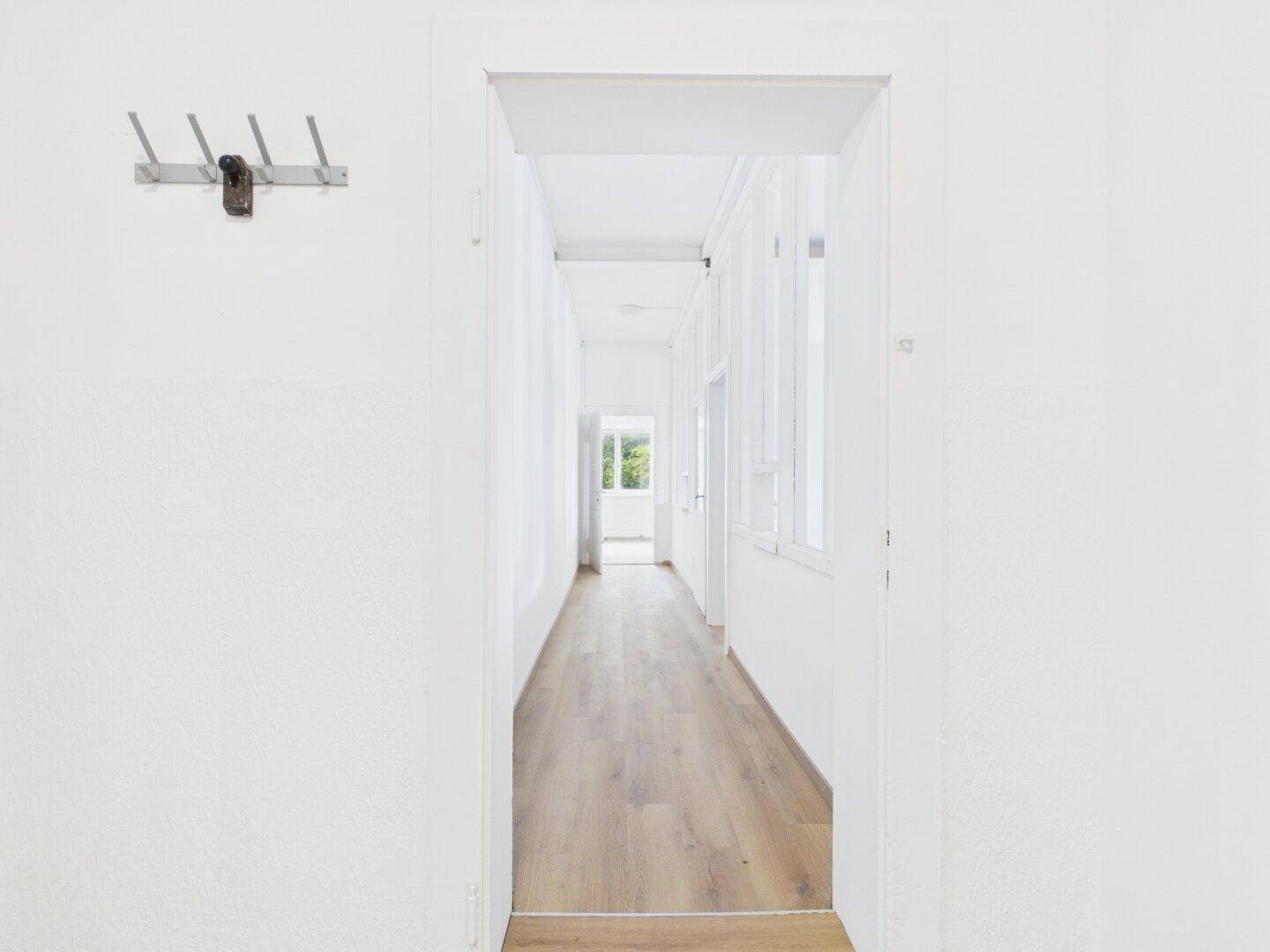 Heller Flur mit weißen Wänden und Holzboden, ausgestattet mit einer Garderobe und viel Tageslicht.