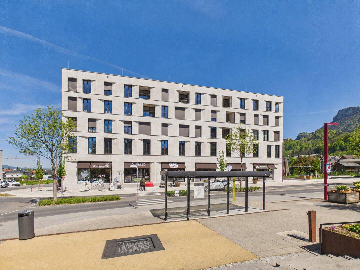 Gesamtansicht eines modernen Geschäfts- und Wohngebäudes mit klarer Architektur und Bergblick im Hintergrund.