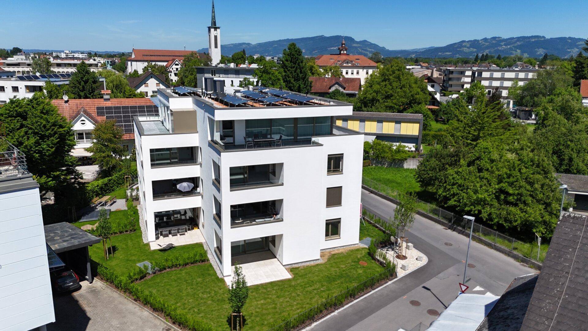 Neubau-Mehrfamilienhaus mit Photovoltaikanlage auf dem Flachdach und Bergblick.