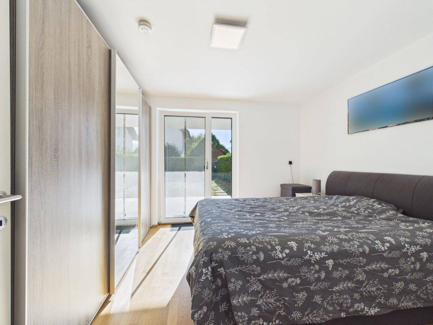 Geräumiges Schlafzimmer mit Holzboden, großem Kleiderschrank und Zugang zum Garten.