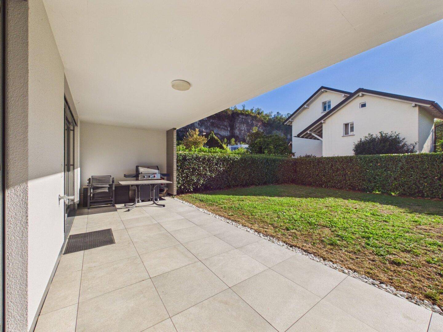 Überdachte Terrasse mit Fliesenboden, Grillbereich und Blick auf den Garten.