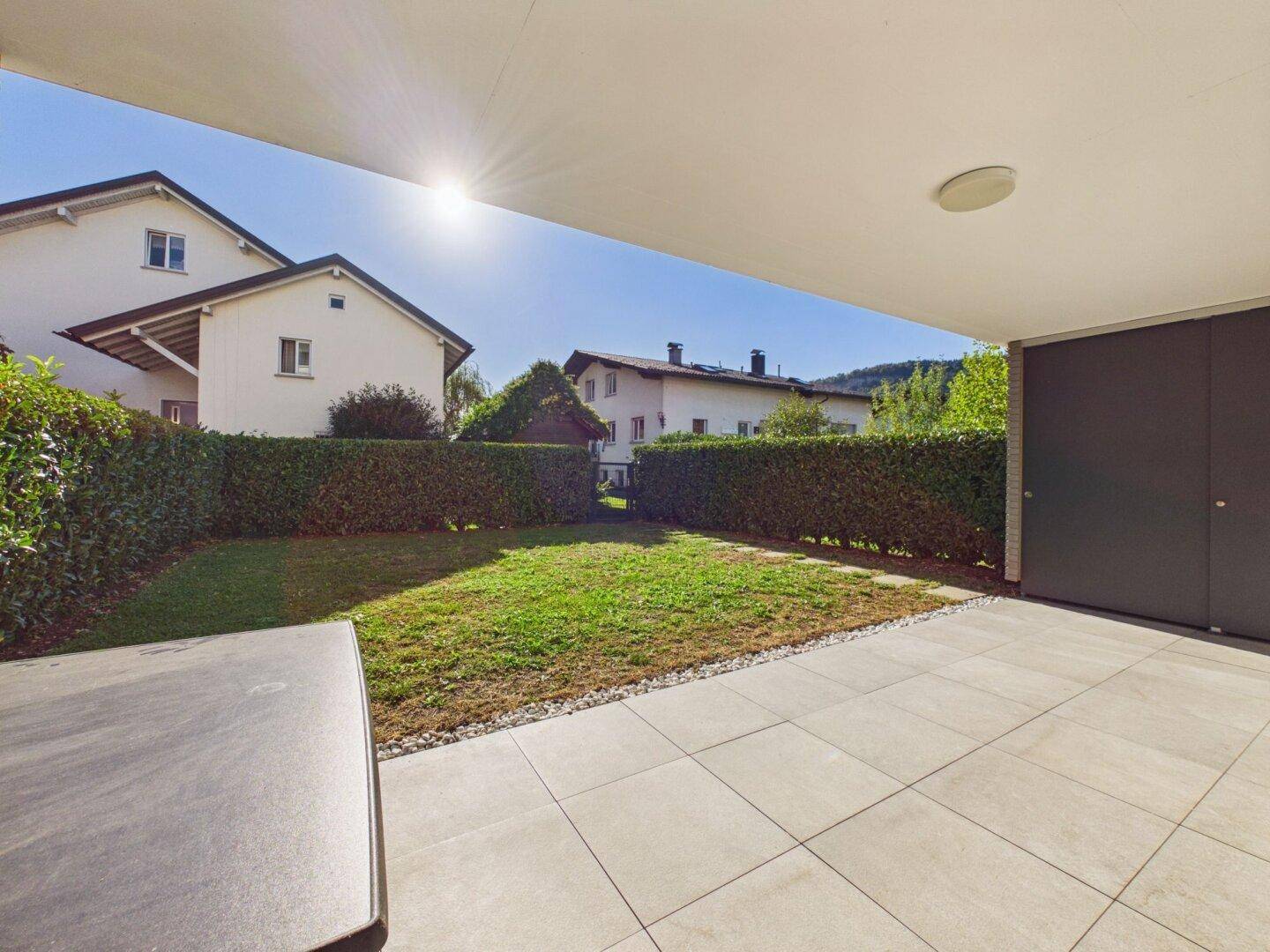 Sonniger Gartenbereich mit Rasenfläche, Hecke und angrenzender Terrasse.