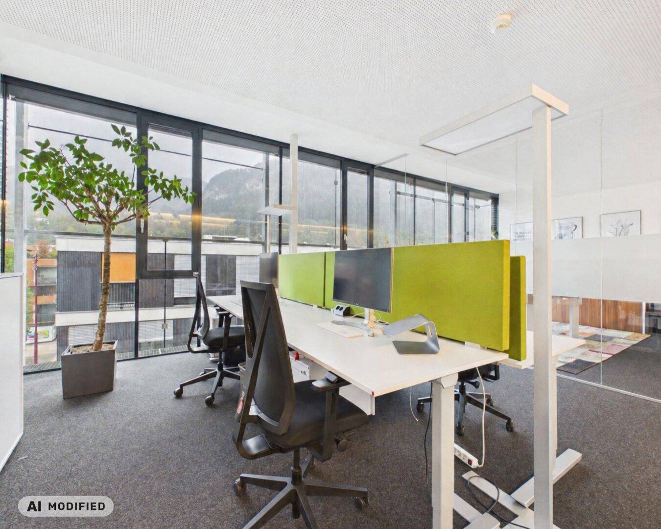 Offener Bürobereich mit modernen Steh-Sitz-Schreibtischen und Blick auf die Berge.