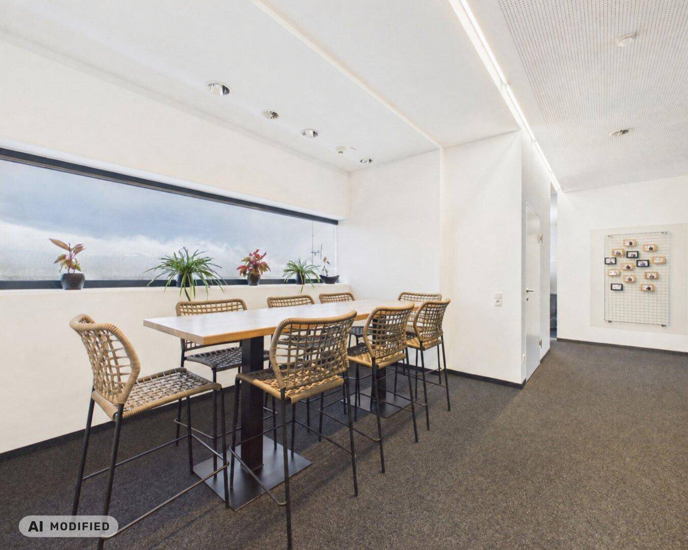 Essbereich im Büro mit Hochtisch und Stühlen, beleuchtet durch ein schmales Fensterband.