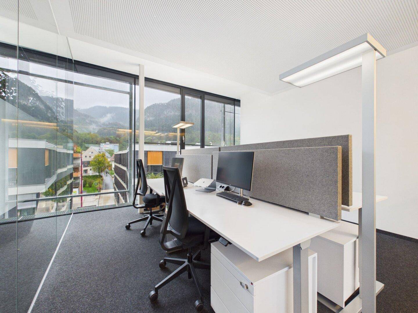 Arbeitsplätze in einem hellen Büro mit großen Fenstern und Blick auf die umliegende Landschaft.