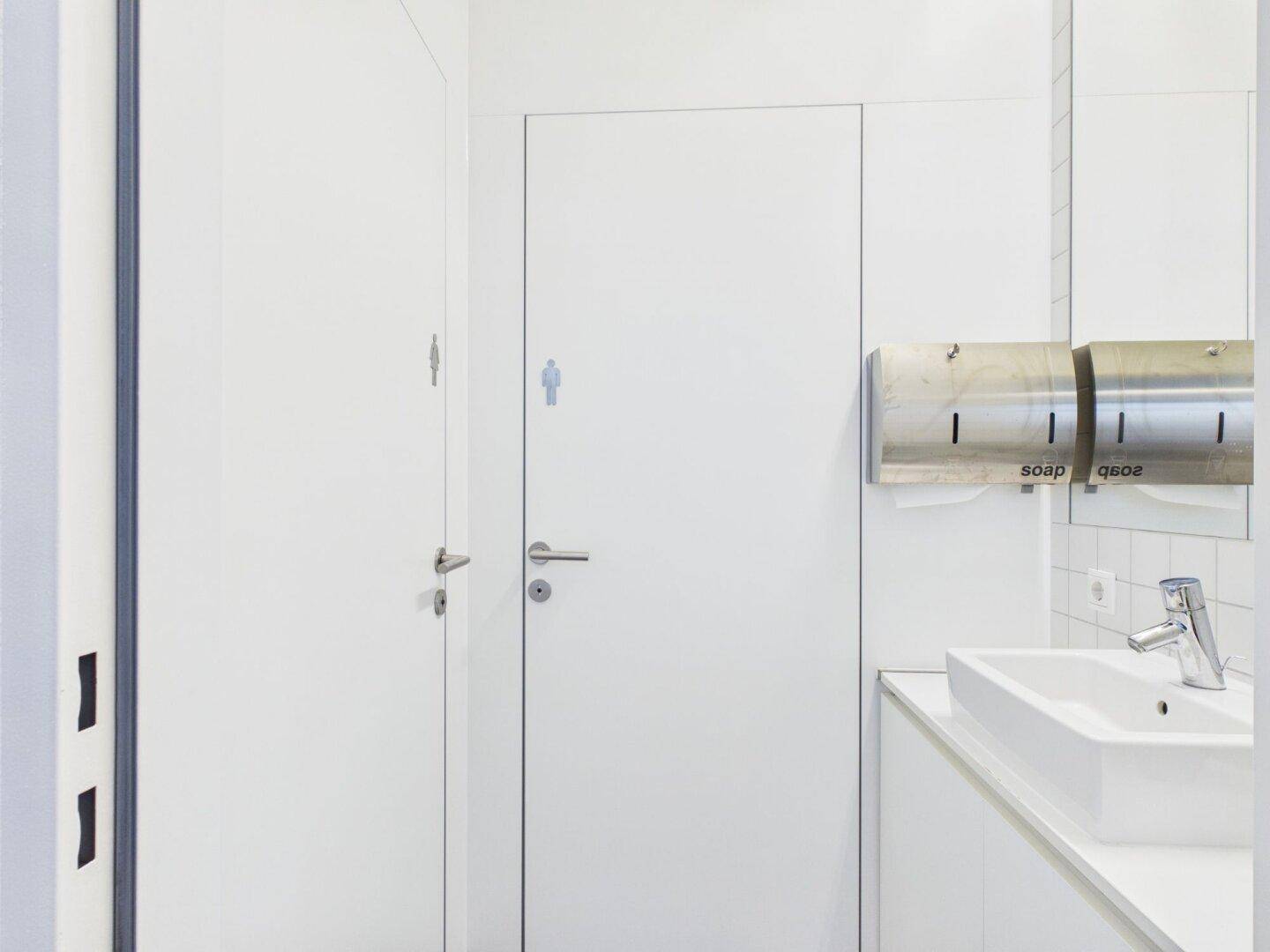 Moderner Toilettenbereich mit weißen Türen, Waschbecken und Seifenspender.