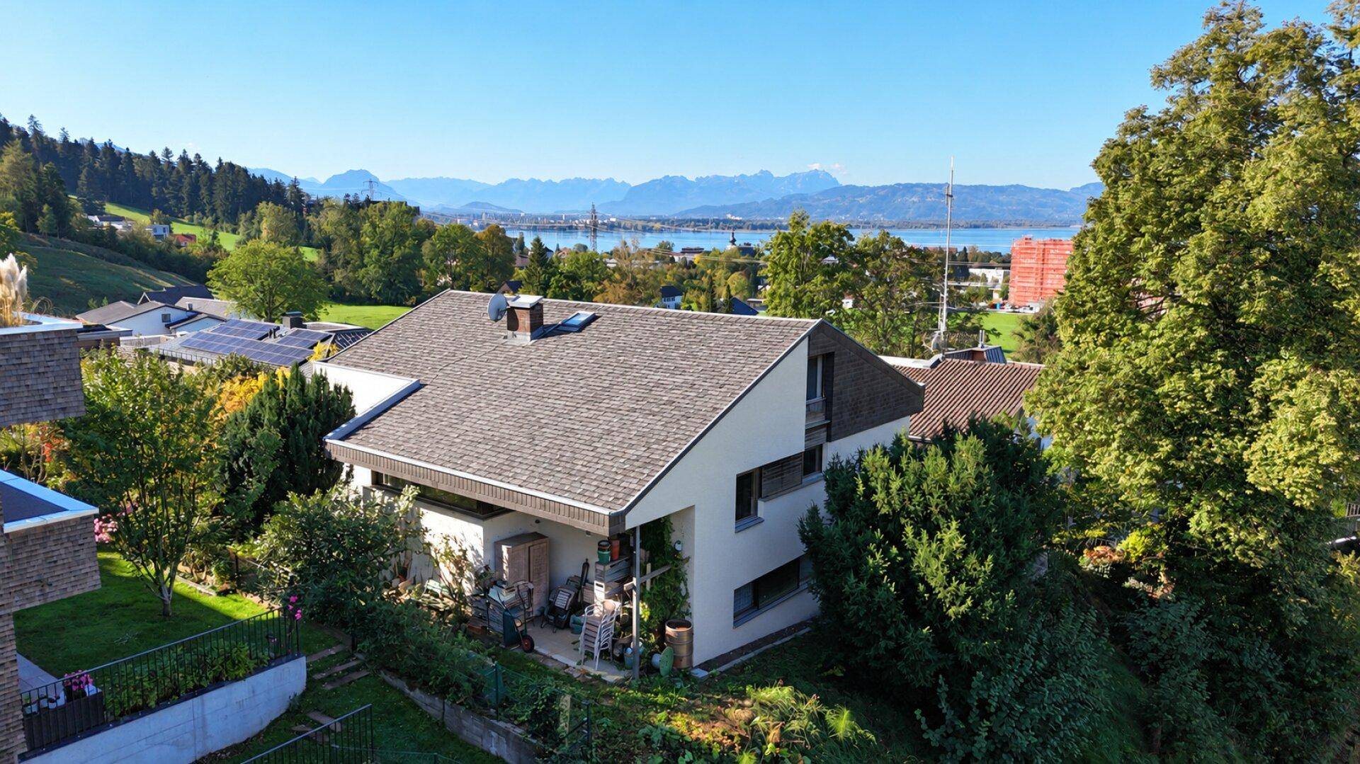 Einfamilienhaus mit Satteldach in grüner Umgebung, mit See- und Bergblick im Hintergrund.