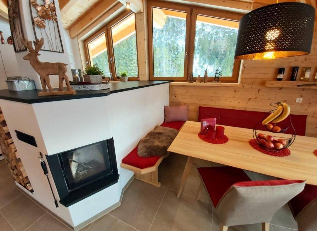 Essbereich mit Kamin, Holzwänden und Blick auf die verschneite Natur durch große Fenster.