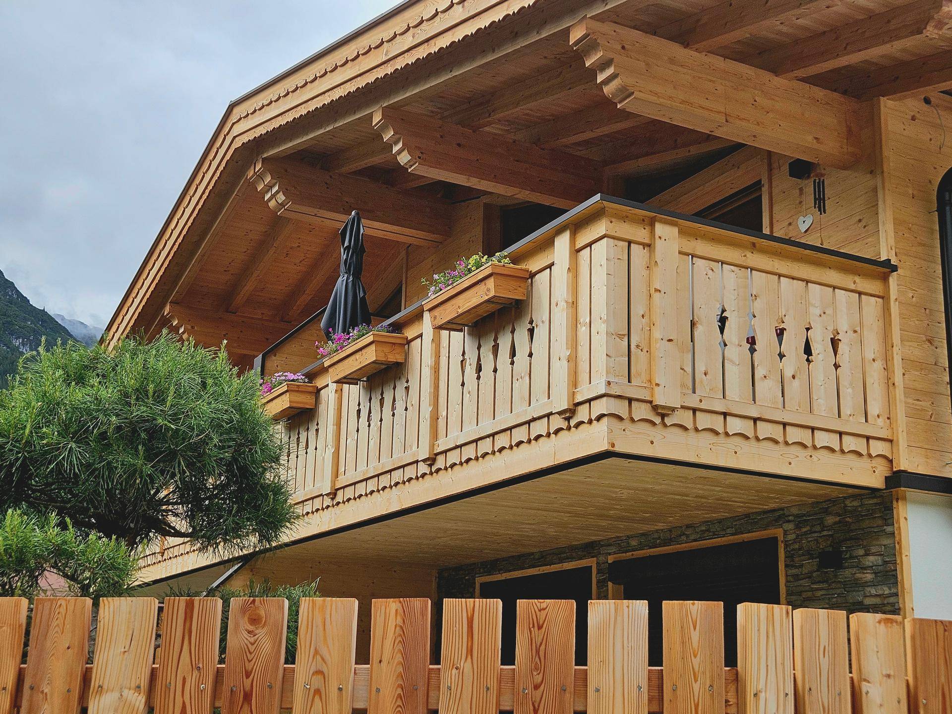 Holzbalkon eines Chalet-Stil Hauses mit traditionellem Geländer und Blumenkästen unter bewölktem Himmel.