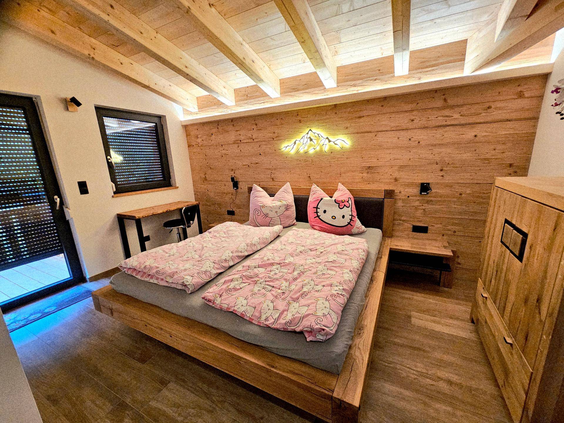 Schlafzimmer mit Holzwänden und -decke, einem großen Bett und dekorativer Neonbeleuchtung.
