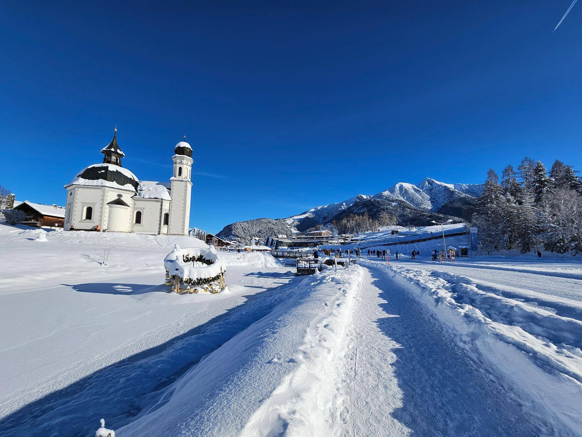 Malerische Winterlandschaft mit einer Kirche und schneebedeckten Bergen unter blauem Himmel.